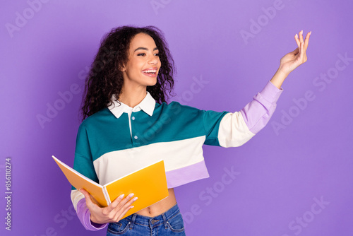 Portrait of lovely young girl hold book talk empty space wear shirt isolated on purple color background