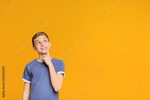 Tricky boy thinking about some prank, looking up at free space on orange background