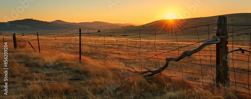 Sunset over rural field with barbed wire fence and mountains in the background, serene landscape. Countryside tranquility and nature concept