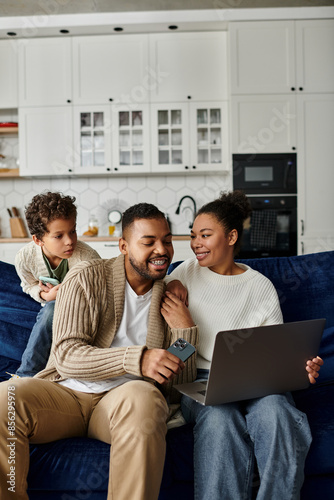 African american family collaborating on a laptop while sitting on a blue sofa.