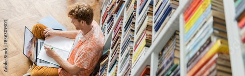 A man, deep in concentration, writes in a library.