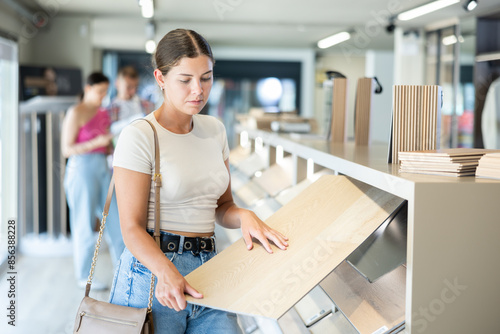 Young woman buyer chooses sample of laminate flooring in hardware store