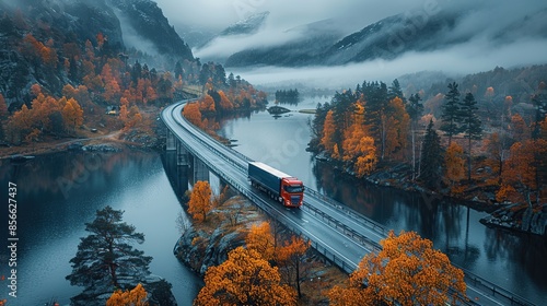 Aerial view of a red truck driving through a misty forest on a winding road surrounded by autumn.