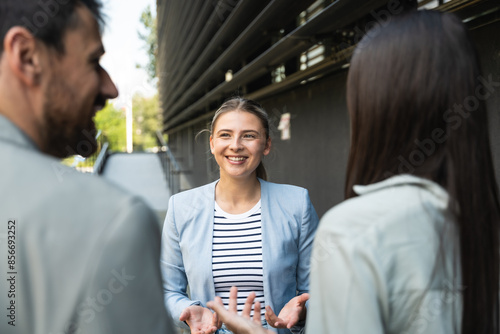 Group of successful young business people, leaders in marketing and motivation, stand in front of office building and consult before a meeting with employees. HR communication in companies concept