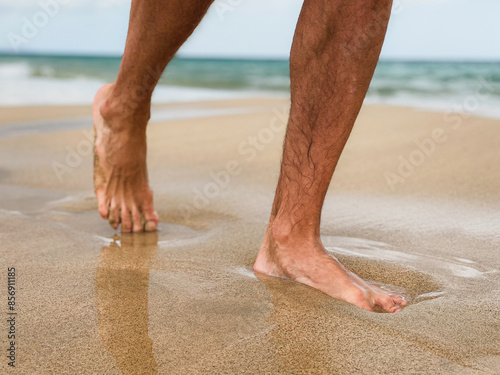 Stopy mężczyzny chodzącego po piasku i falach morskich. Mężczyzna spacerujący boso po plaży. 