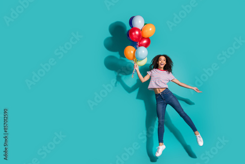 Full length photo of lovely young lady hold air balloons jump dressed stylish striped garment isolated on cyan color background