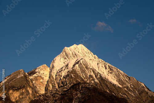 cima inneva di una montagna molto alta, nell'Italia nord orientale, in inverno, illuminata di arancione dalla luce del sole al tramonto, sotto un cielo sereno