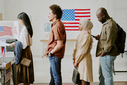 Medium long side view shot of ethnically diverse young people standing in line to get ballot papers at voting station