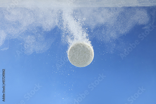 Effervescent pill dissolving in water on blue background, closeup