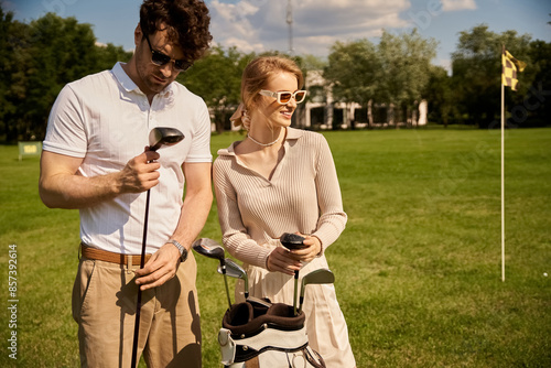 A young couple, elegantly dressed, stands together on a picturesque golf course, embodying a classic, upper-class lifestyle.