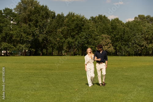 A beautiful young couple in elegant attire taking a leisurely walk together in a picturesque park setting.