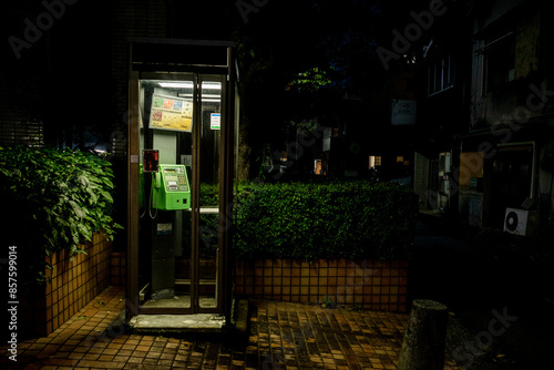 A typical japanese green coin-operated public telephone inside a booth at night at Numazu, Shizuoka.