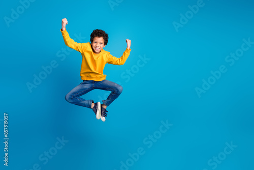 Full body photo of cute little boy jump winning raise fists dressed stylish yellow clothes isolated on blue color background