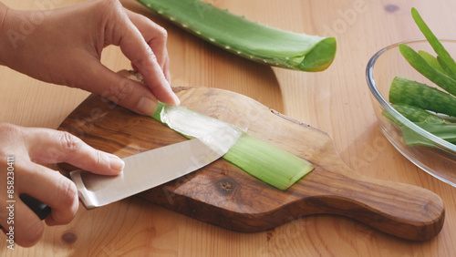 Slicing and separating aloe vera gelly flesh from leaf with knife on wooden table.