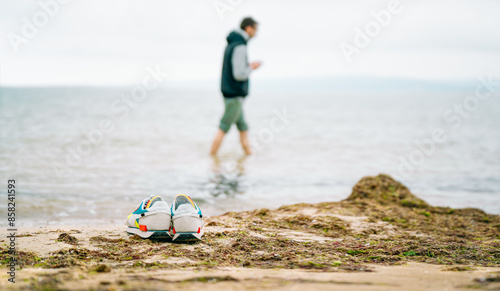 Colorful shoes on sandy beach with person walking in shallow water in the background