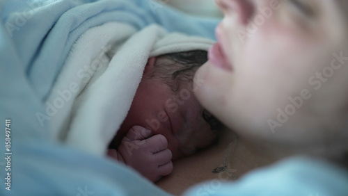 Newborn baby resting on mother's chest right after birth emphasizing skin to skin contact, real life authentic infant covered by blankets to keep warm in postpartum