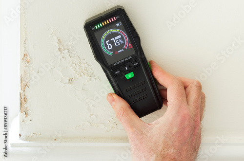 Moisture meter against a wall with rising damp, UK home interior