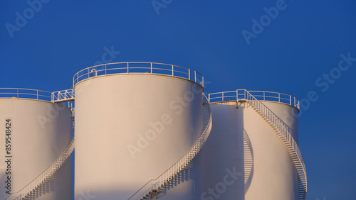 Three white storage fuel tanks in oil industrial area against blue clear sky background