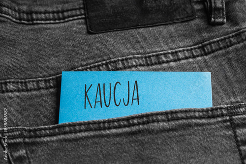 Blue card with a handwritten inscription "Kaucja", inserted into the pocket of gray pants jeasnow (selective focus), translation: Bail