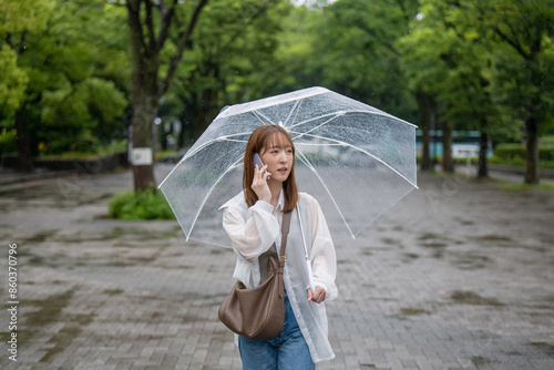 電話で話しながら雨の公園を歩く女性