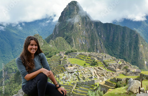 Attractive young Latina brunette woman with long hair sitting in the ruins of Machu Picchu and happy after arriving at one of the seven wonders of the world wearing sports clothes