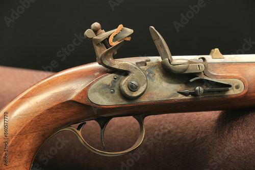 Close-up of the trigger and flintlock with the mounted flint and closed tinder on the black background. Kentucky flintlock pistol.