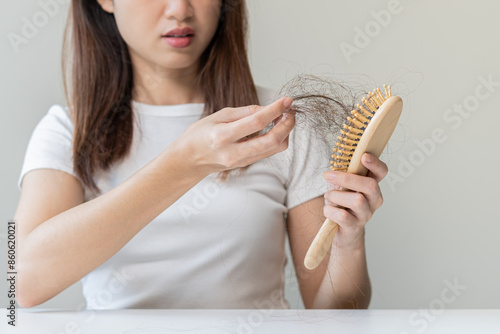 Serious asian young woman holding brush holding comb, hairbrush with fall black hair from scalp after brushing, looking on hand worry about balding. Health care, beauty treatment, hair loss problem.