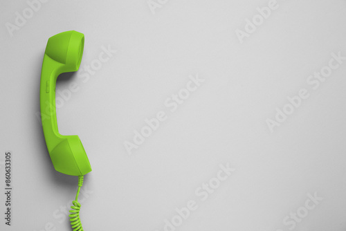 Green telephone handset on light background, top view. Space for text