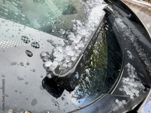 Close-up of a car windshield covered in hailstones and raindrops, highlighting the aftermath of a hailstorm with ice pellets accumulated around the windshield wiper