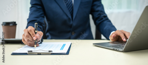 A banker in a suit works at a desk handling loans, analyzing client financial data, providing financial advice, dealing with stocks and the stock market, and studying economic situations.