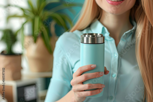 Woman holding thermos bottle at workplace, closeup