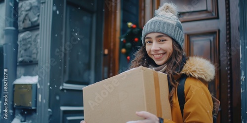 A woman wearing a hat and a brown coat is holding a brown cardboard box. She is smiling and she is happy