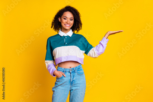 Photo of positive woman with perming coiffure dressed stylish shirt plam presenting empty space isolated on yellow color background