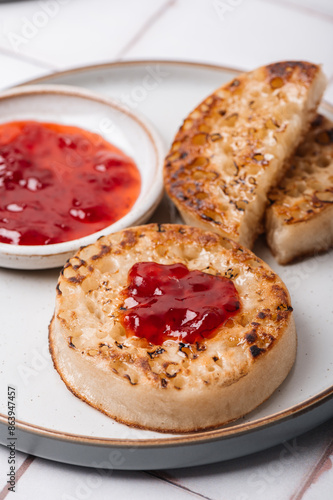 Hot Toasted Crumpets with piece of butter on a plate with strawberry jam. Perfect tasty breakfast popular in England, UK