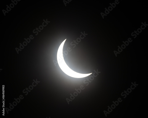 Partial solar eclipse with moon blocking sun, sun shining in a crescent shape in black sky