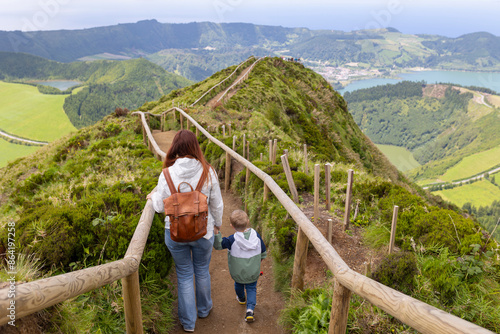 A woman and a child are walking on a path in a lush green area