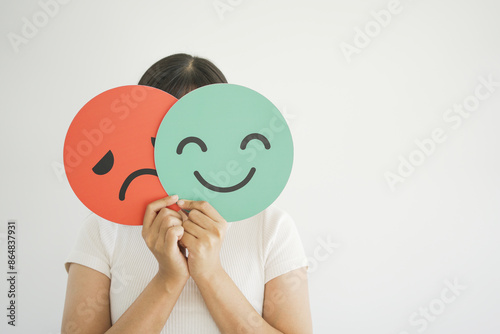 Woman hands holding sad face hiding behind happy face, bipolar and depression, mental health, split personality, mood change concept