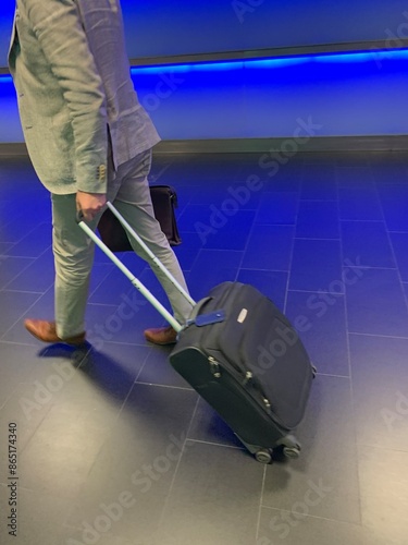 gestresster Mann im Business Anzug zieht schwarzen Koffer am Bahnhof / Flughafen