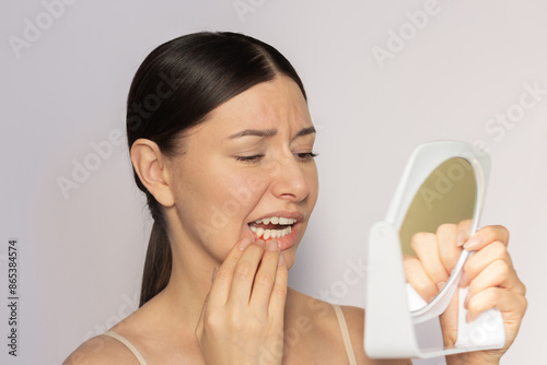 Young pretty caucasian woman looking at her red gums on her lower jaw in the mirror. She suffering from gingivitis, gum inflammation. Dental care. Dentistry. Oral care