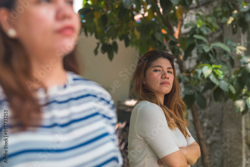 A woman intensely scrutinizes another woman with a jealous expression outdoors. Giving the side eye. Depicts rivalry, suspicion, and interpersonal conflict.