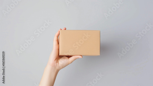 Mockup Woman's hand holds a brown rectangular cardboard box on a light gray background. Ai Generated Images