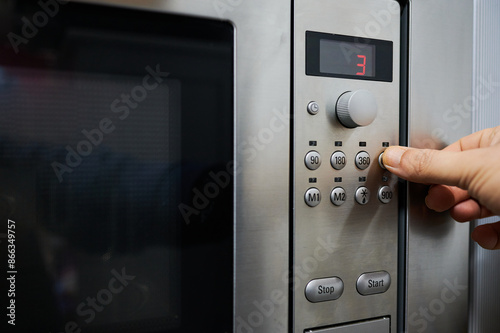 Hand of an unrecognizable person operating the microwave, pressing the button to select the microwave power with a finger.