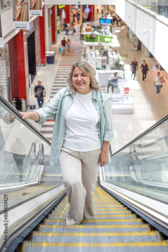 Overweight woman in a shopping center makes purchases, while is standing on moving staircase.