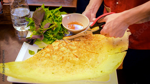 A waiter slices a crispy Banh Xeo to serve to diners. Vietnamese crepe