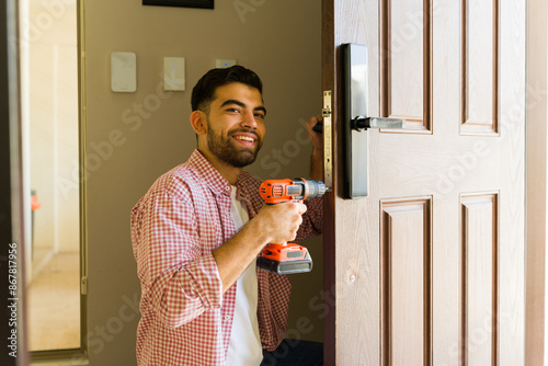 Smiling handyman installing a new door lock on a wooden front door using a power drill