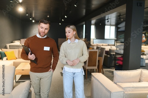 Young salesman helping customer to choose new modern sofa in store