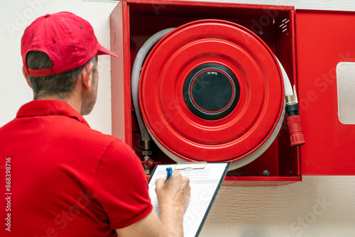 Technician performing inspection of fire hose cabinet. Fire protection systems maintenance for safety.