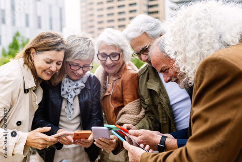 Senior group of people using mobile phone device standing in circle outdoors. Technology and baby boomers lifestyle concept