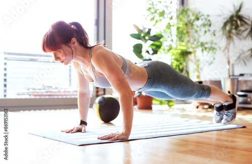 Beautiful redhead woman's home fitness routine, doing pushups. Home workout on gym mt in living room, sporty woman wearing sportswear.