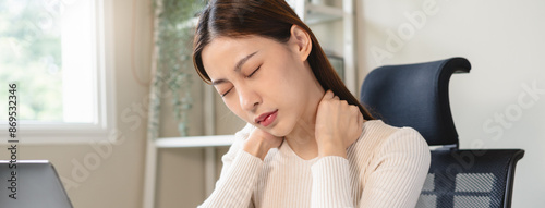 Asian business woman suffering from neck pain working in office sitting at table.